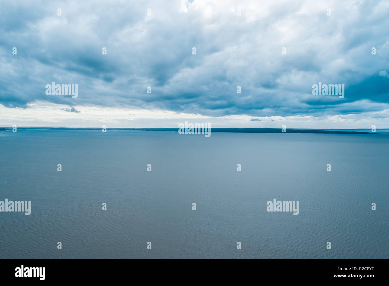 Antenne Seascape - Regen Wolken über ruhigem Wasser und kleinen Flecken Land am Horizont - Ruhige bedeckt Szene Stockfoto