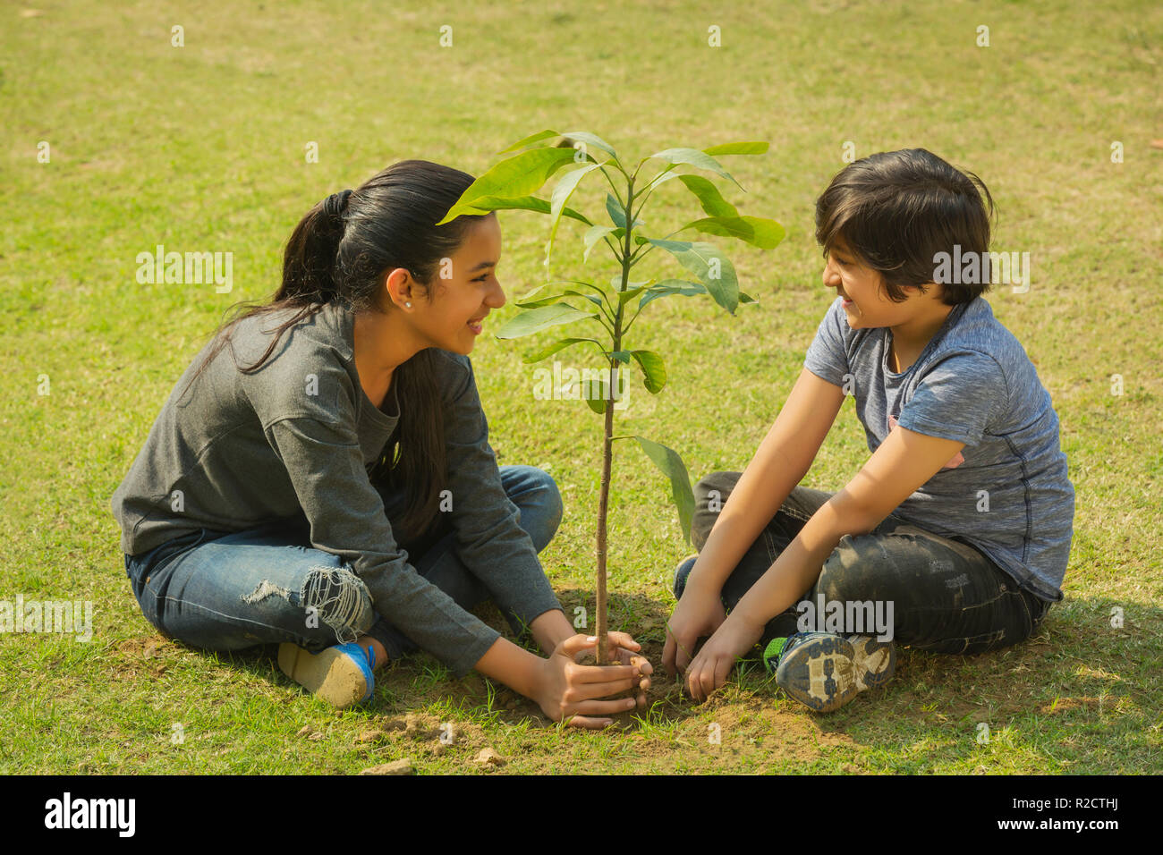 Lächelnd Bruder und Schwester das Einpflanzen einer kleinen Pflanze im Garten sitzen auf dem Boden. Stockfoto