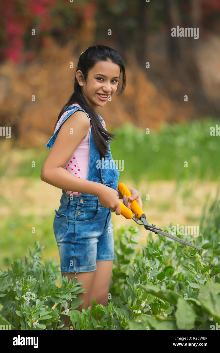 Glückliche junge Mädchen schneiden von Pflanzen im Garten mit einer Hecke Scherung oder Gartenarbeit Schere. Stockfoto