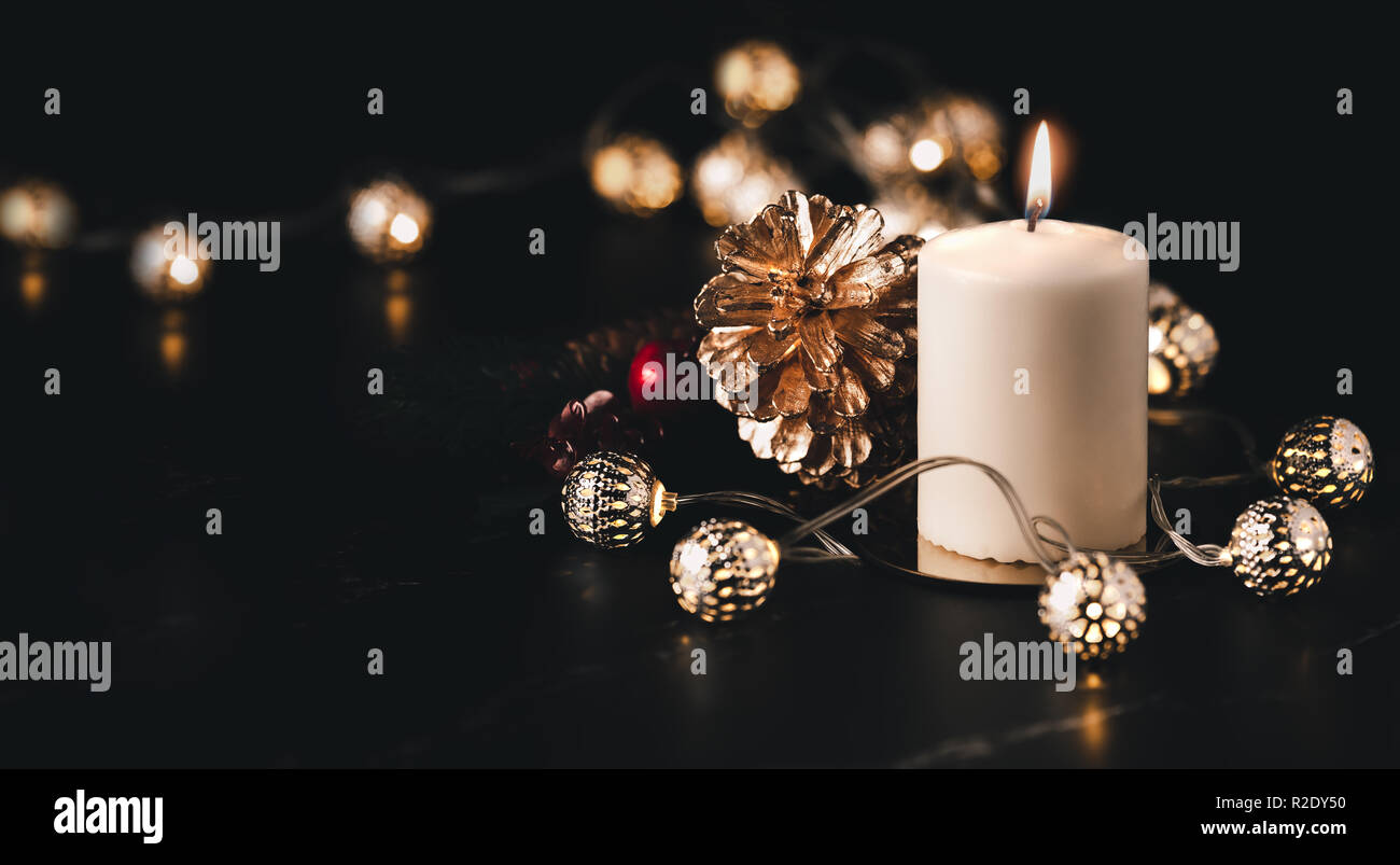 Weihnachten weiße Kerze mit goldenem Pine Cone, Mistel und Licht string auf schwarzem Marmor tisch mit dunklen Hintergrund leuchten. Urlaub Grußkarte Stockfoto