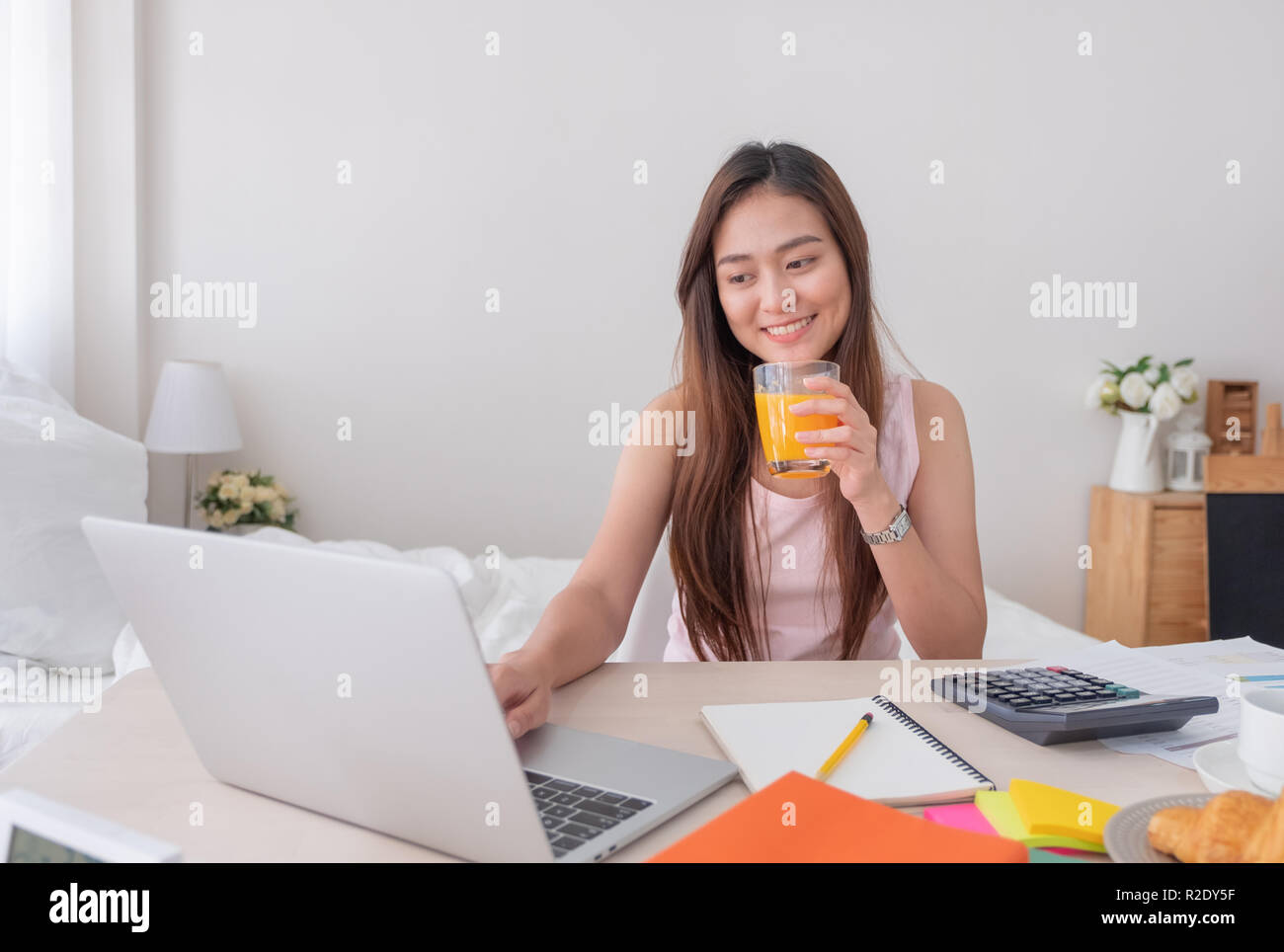 Asiatische Frau Freiberufler trinken Orangensaft und und Arbeiten am Laptop zu Hause. Arbeit zu Hause Konzept. Arbeiten von zu Hause Konzept Stockfoto
