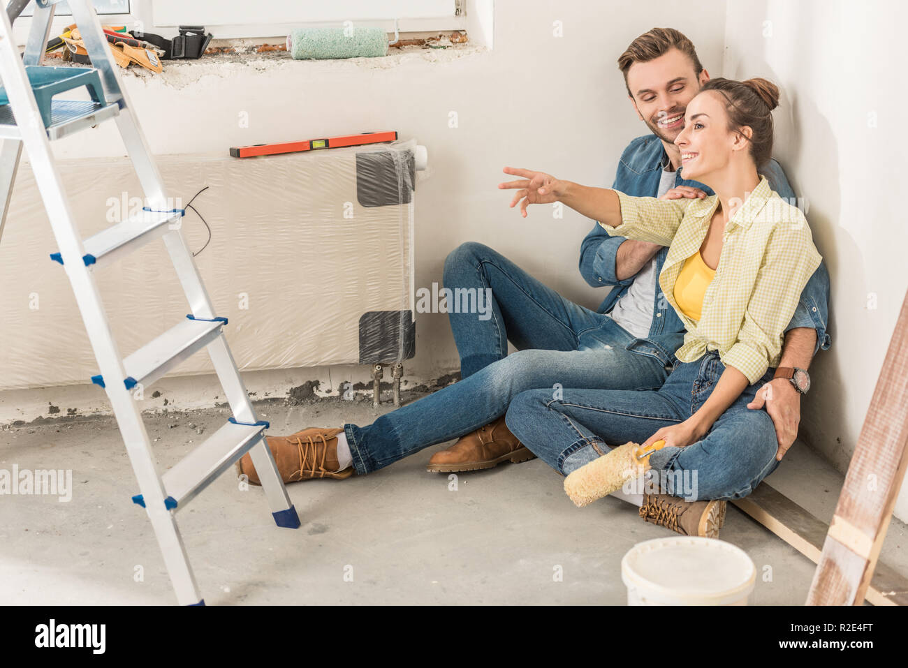 Glückliches junges Paar sitzen auf dem Boden und weg schauen während home improvement Stockfoto