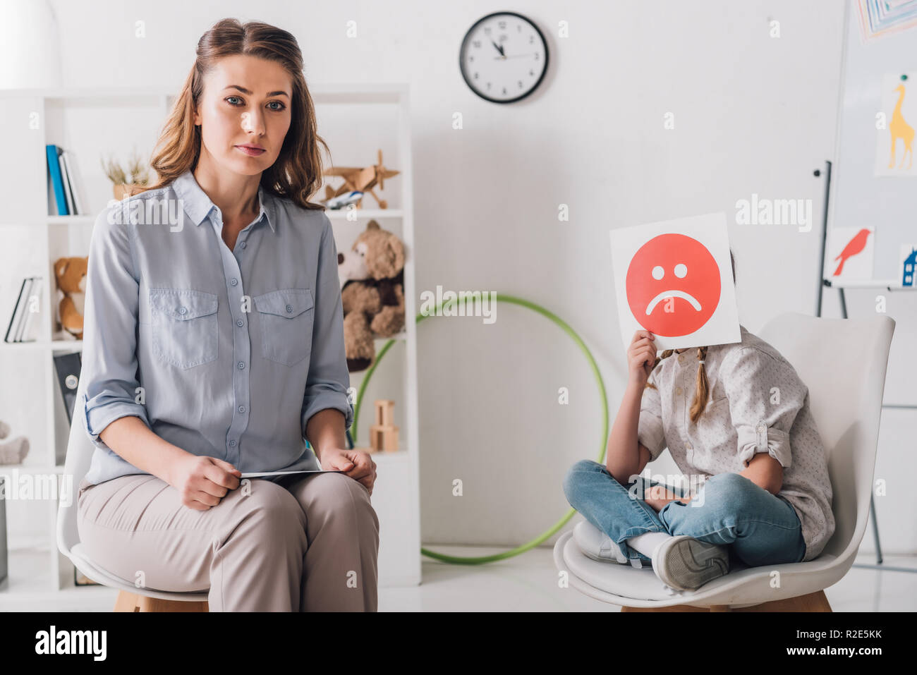 Psychologe sitzen in der Nähe von kleines Kind, während Sie das Gesicht mit einem traurigen Gefühl Gesicht Karte Stockfoto