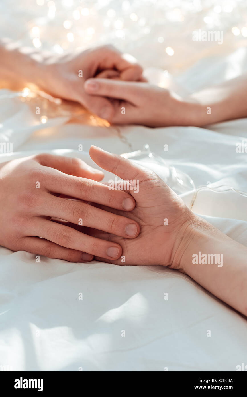 Teilweise mit Blick auf die paar Hände halten, während im Bett liegend mit Girlande Stockfoto