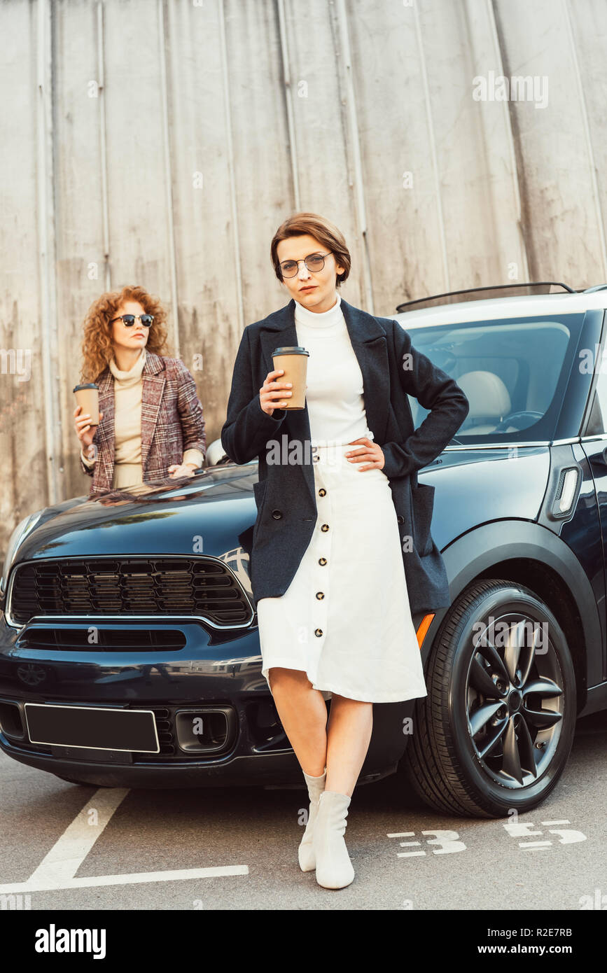 Modische weibliche Modelle in Mäntel mit Einweg Kaffeebecher in der Nähe  Auto an Urban Street posing Stockfotografie - Alamy