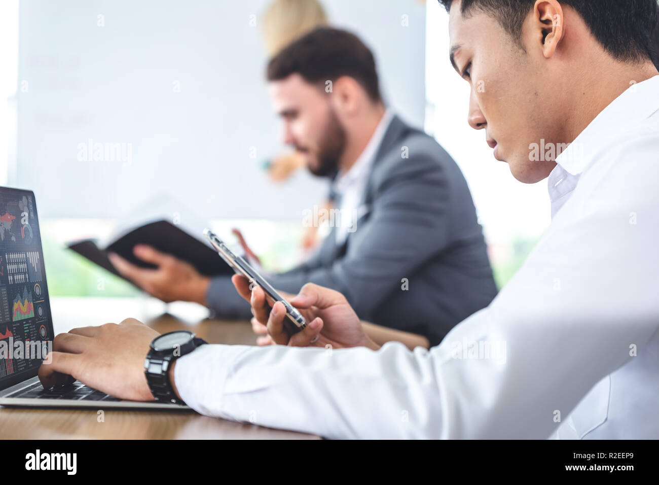Business mit männlichen Technologie Laptop mit Smartphone, während andere mit alten Papier Bericht im Tagungsraum. Stockfoto