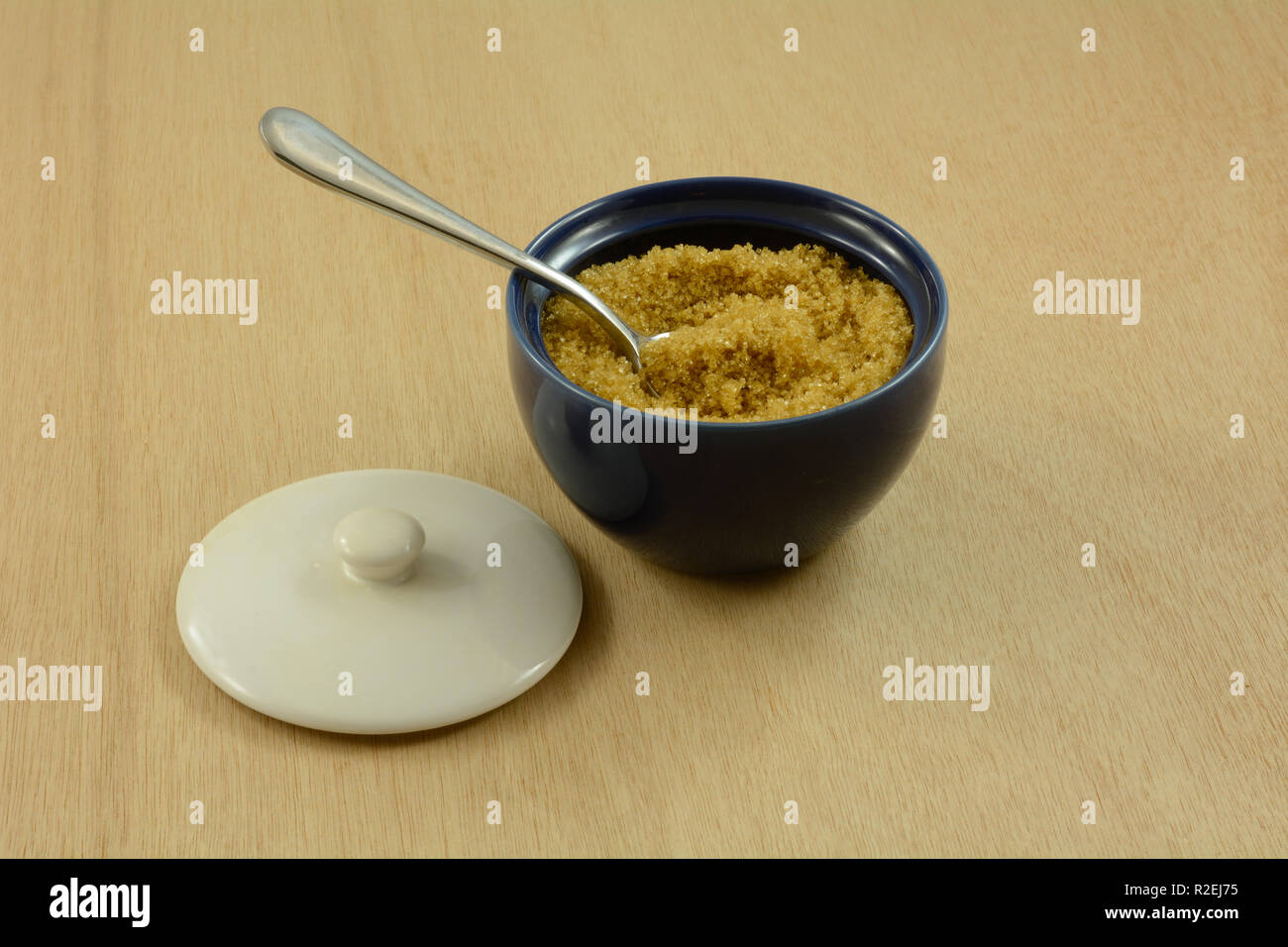 Brauner Zucker in blau Zuckerdose mit Löffel innen weiß Deckel und an hölzernen Tisch Stockfoto