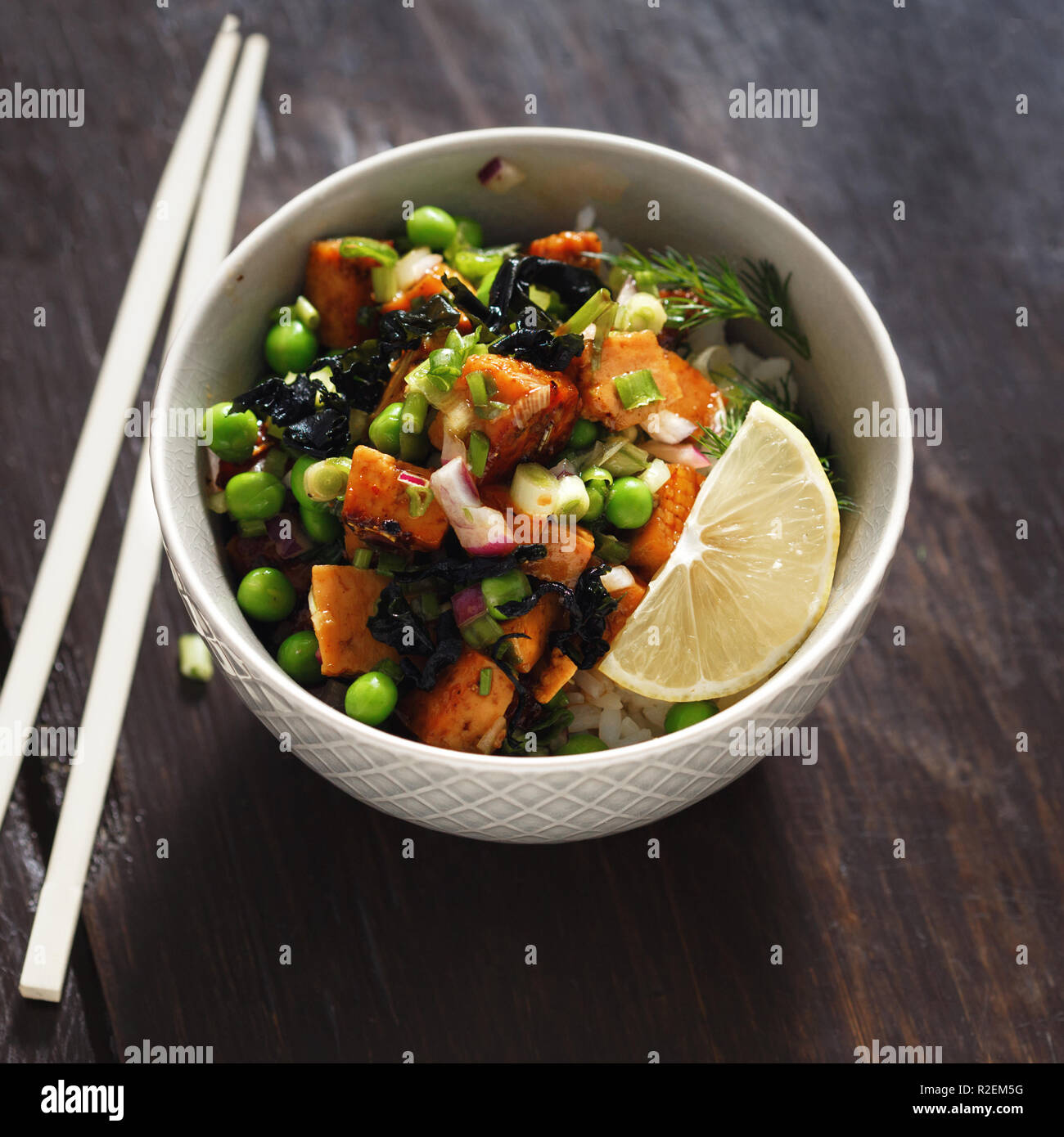 Schüssel mit Tofu, Reis, Seetang, grüne Erbsen und Zwiebeln auf Holztisch. Leckere und gesunde vegetarische Kost. Vegetarische poke Schüssel Stockfoto