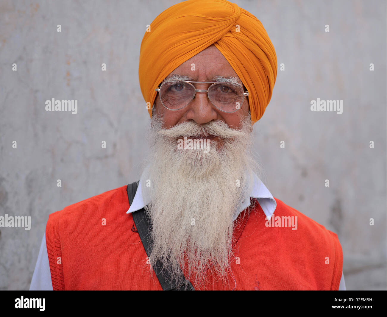 Älteren indischen Sikh Mann mit einem orangefarbenen Turban (Dastar) und aviator Stil Brillen für die Kamera posiert. Stockfoto