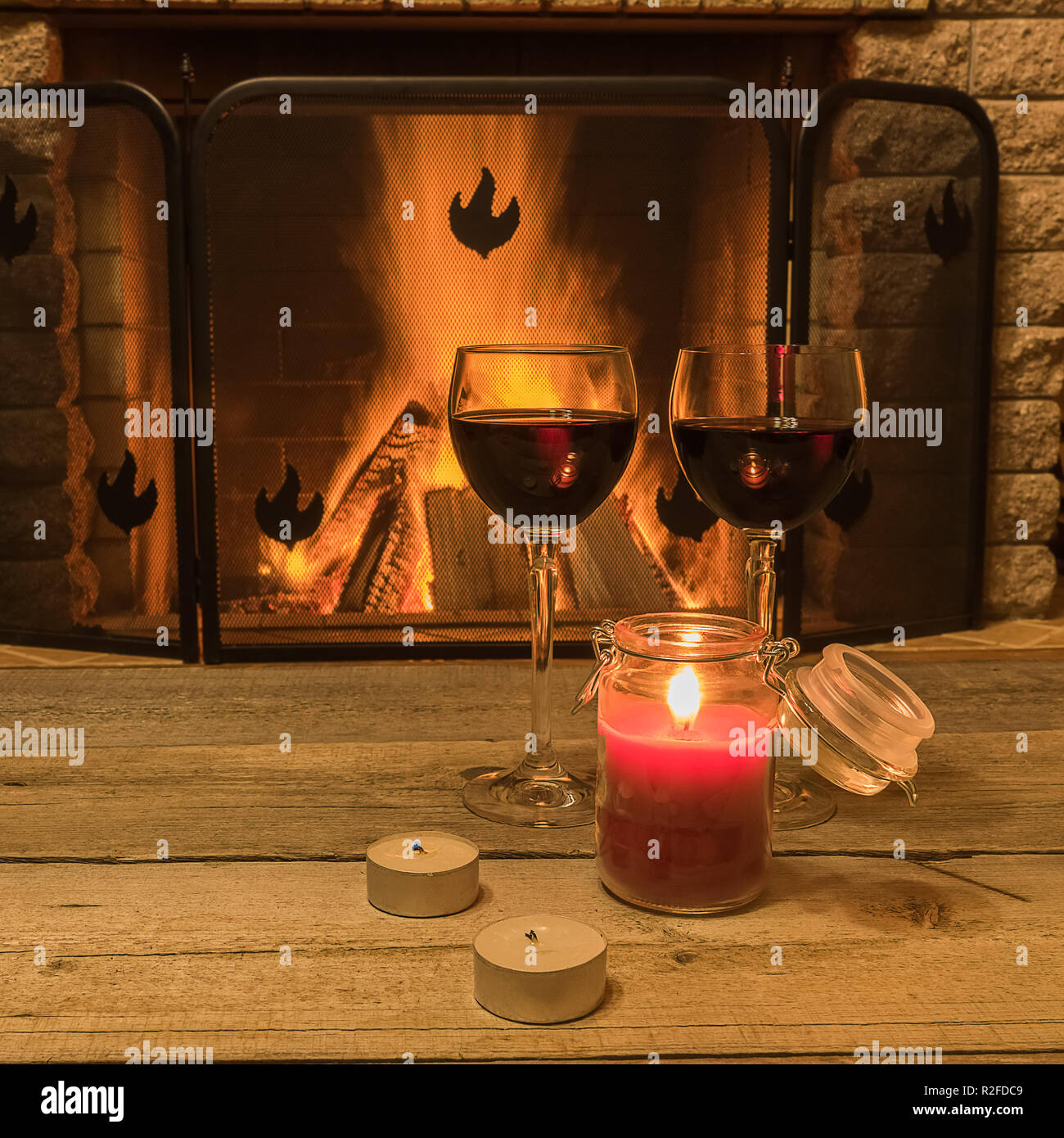 Ruhige Szene vor dem gemütlichen Kamin, mit zwei Gläsern Rotwein und Kerzen, im Landhaus, im Winter Urlaub. Stockfoto