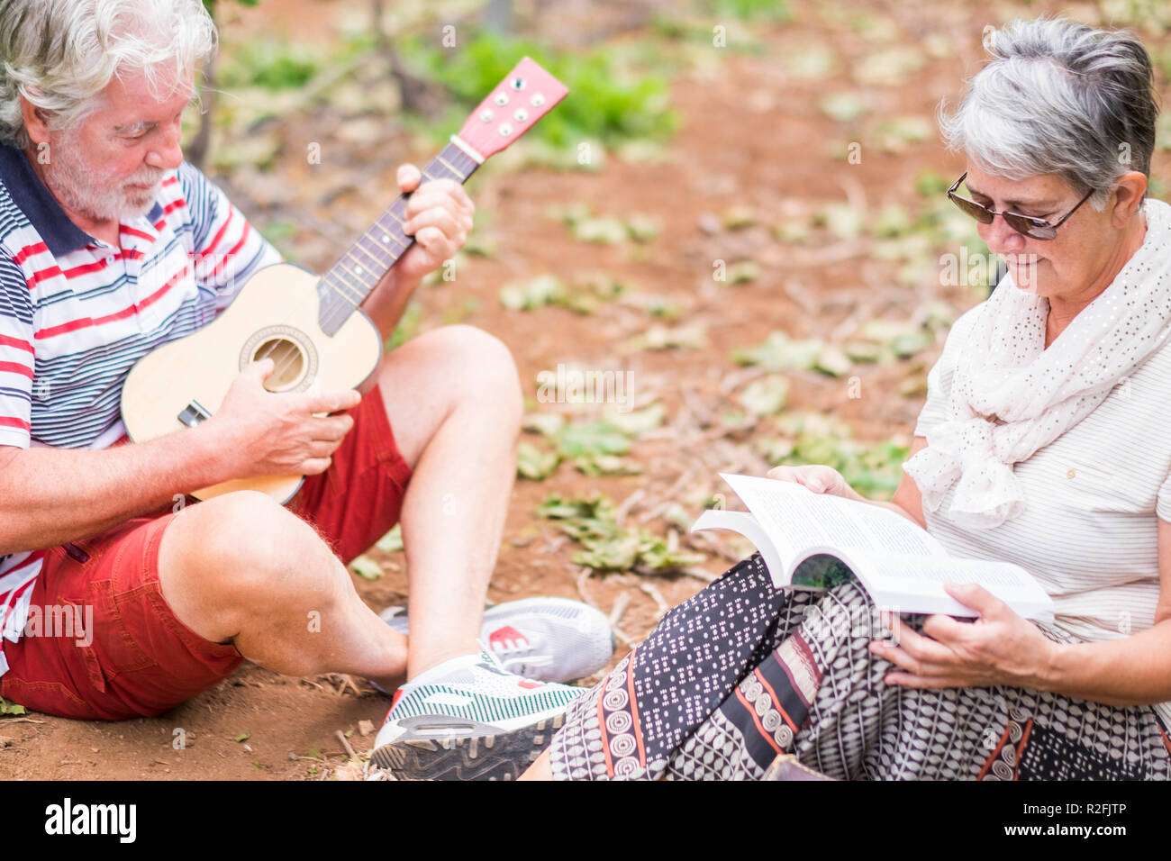 Paar Alternativen im Alter von älteren Reisenden bleiben oder sich in einen Weinberg mit dem Gepäck und spielen eine Ukulele, E-Gitarre und lesen Sie ein Buch aus Papier. einfachen Lebensstil im Freien Plätze und Natur fühlen Stockfoto