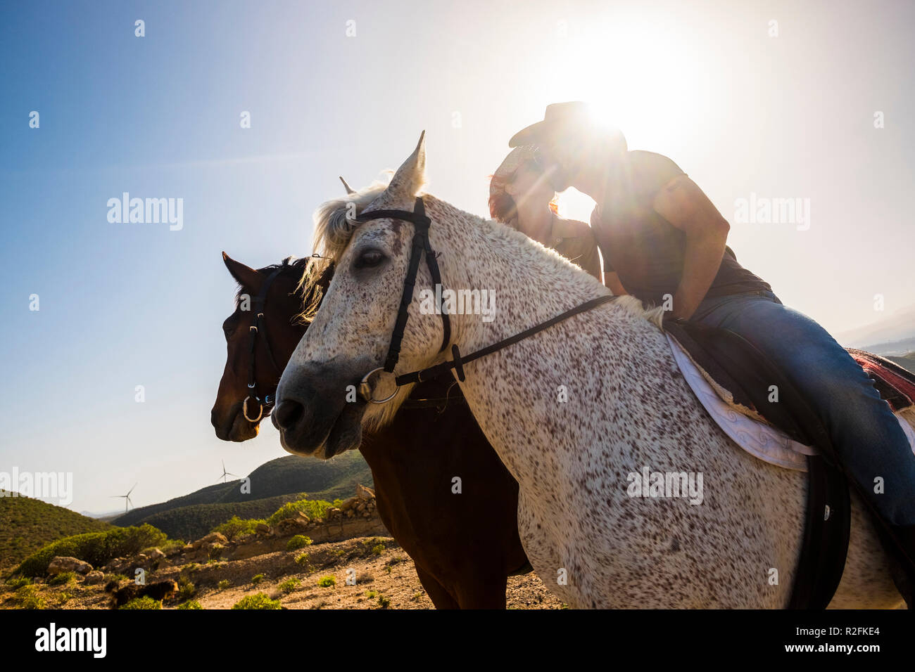 Liebe Szene zwischen junge Schöne coule reiten zwei nette Pferde in der Natur. Windmühle für grüne Energie und bessere Zukunft im Hintergrund. alternative Freiheit und schönen Lebensstil. Moderne cowboy Stockfoto