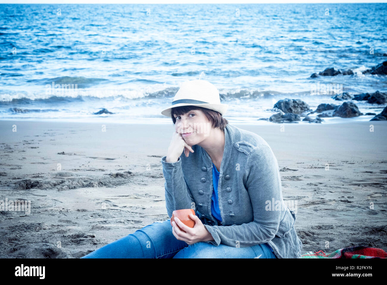 Schöne schöne junge Dame lächelnd mit Hut sitzen am Strand im Winter. Ferienhäuser schöne Freizeitaktivitäten Konzept outdoor. Stockfoto Schöne schöne junge Dame lächelnd mit Hut sitzen am Strand im Winter. Ferienhäuser schöne Freizeitaktivitäten Konzept outdoor. Stockfoto