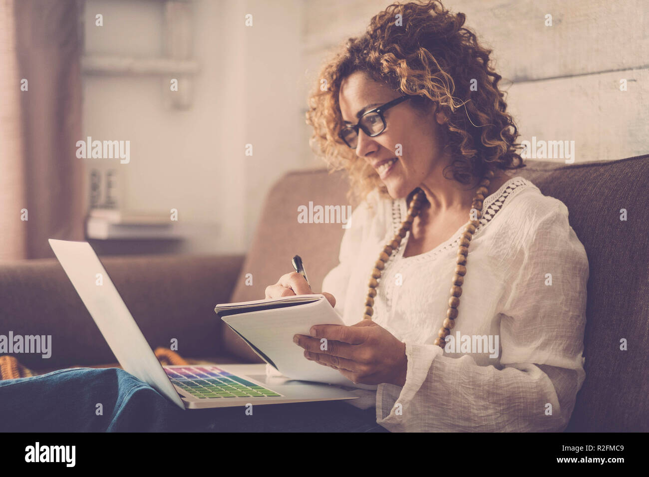 Schöne Frau lächeln und Noten schreiben auf Papier, die an einem Notebook arbeitet Freiheit von Büro zu Hause. alternativen Lebensstil und auf zu arbeiten. Vintage Retro Look. Stockfoto
