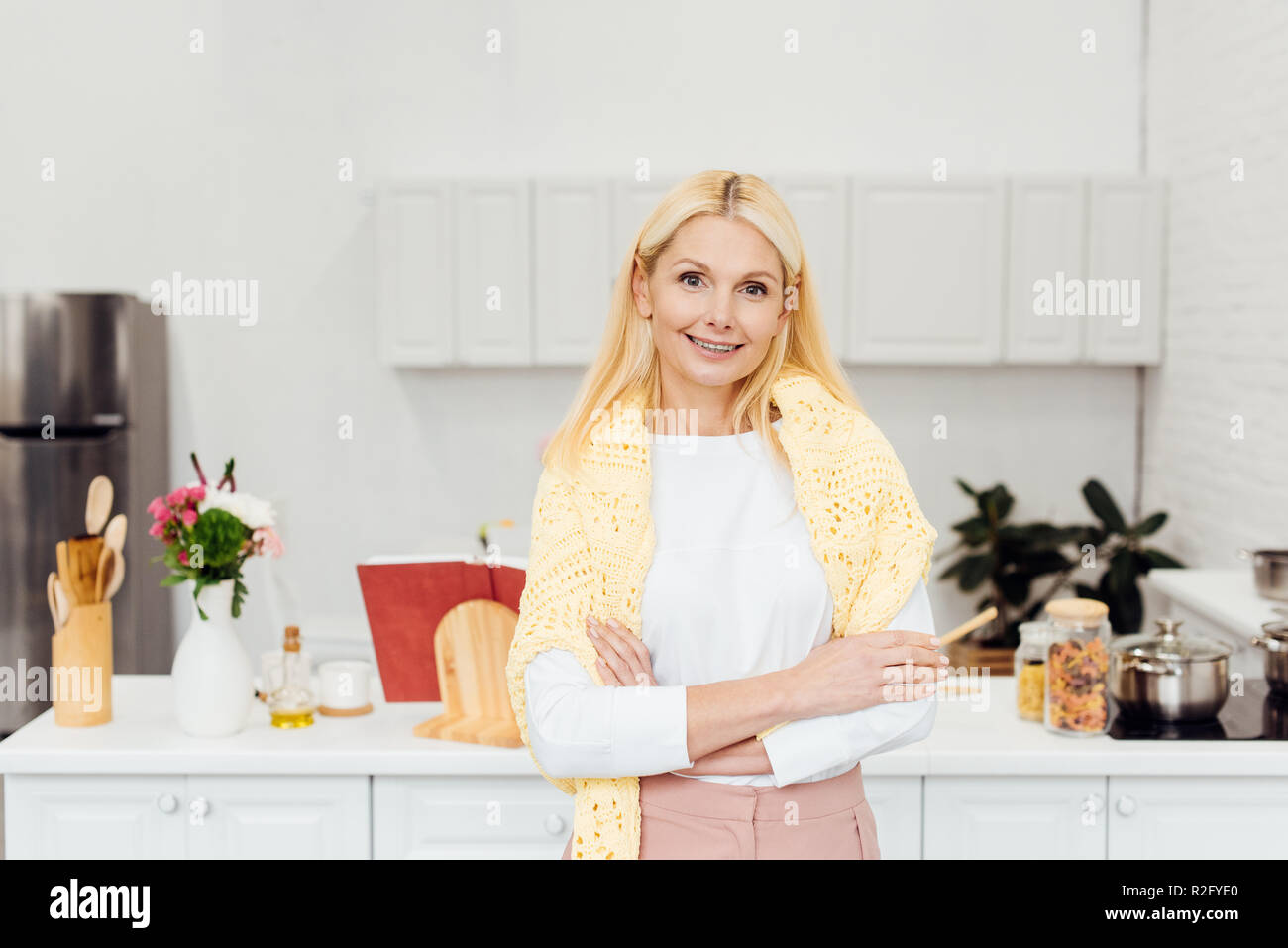 Lächelnde blonde Frau mit gekreuzten Armen stehen in der Küche Stockfoto