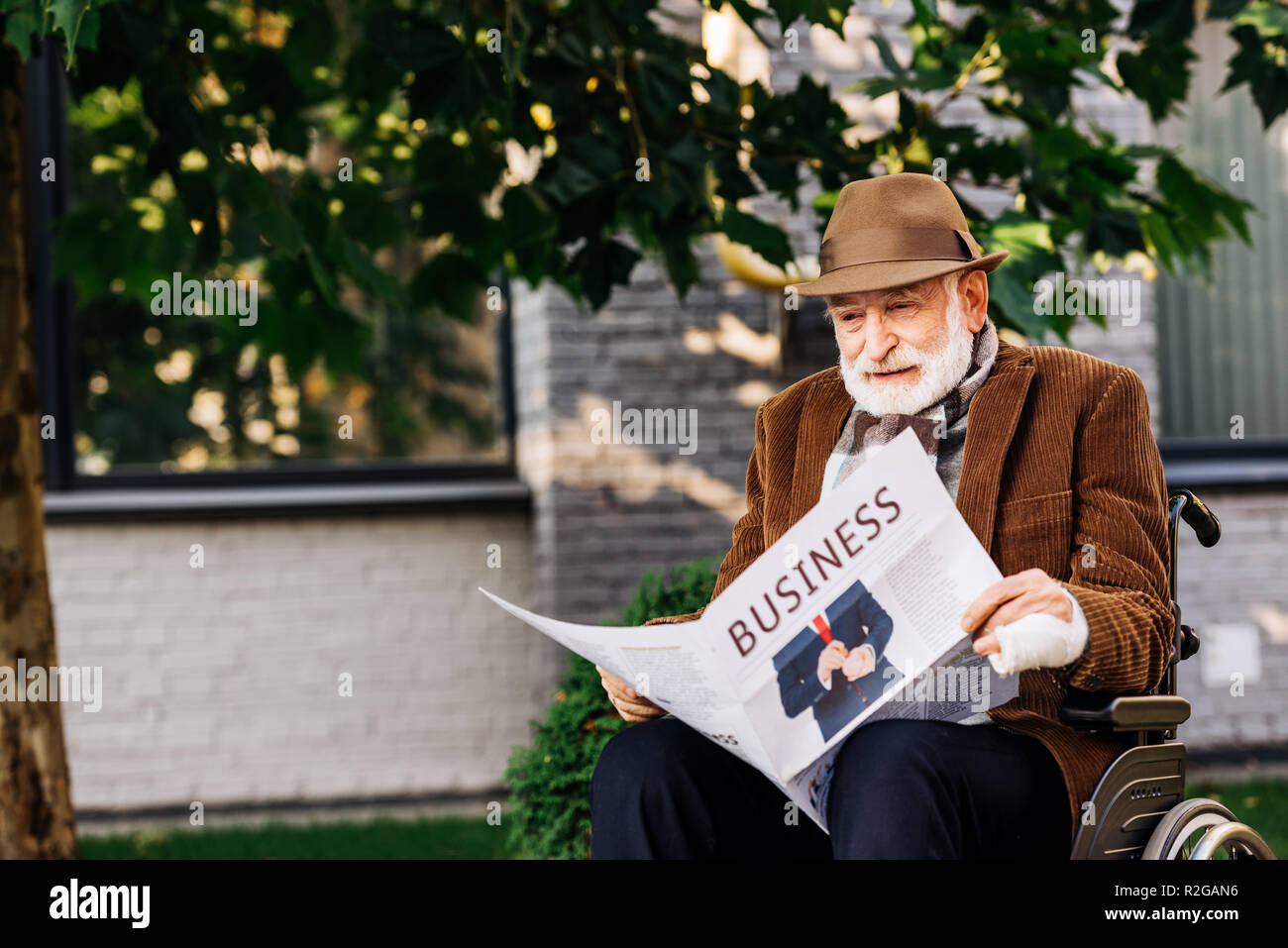 Ältere behinderte Menschen im Rollstuhl lesen Zeitung auf der Straße Stockfoto