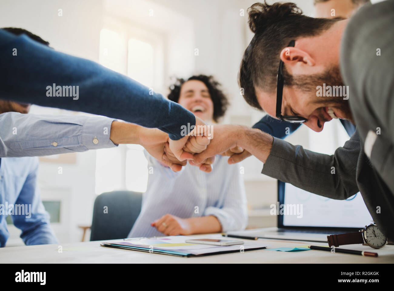 Junge Geschäftsleute sitzen um den Tisch in einem modernen Büro, die Faust zu stoßen. Stockfoto