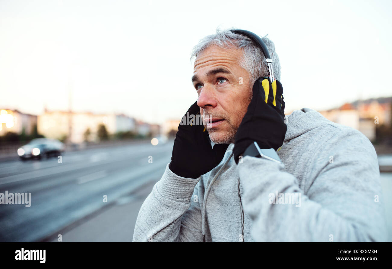 Reife männliche Läufer setzen auf Kopfhörer draußen in der Stadt. Stockfoto