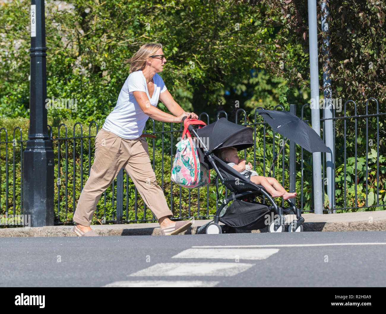 Frau in 30 s oder 40 s Kind schieben Kinderwagen mit Sonnenschutz Sonnenschirm Schatten Zicklein von Sonne, im Sommer in Großbritannien. Stockfoto