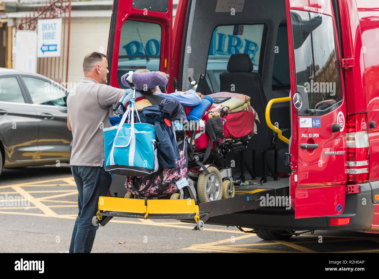 Ein Mann helfen, eine Behinderte benachteiligte Person in die Rückseite eines Fahrzeugs in Großbritannien. Stockfoto