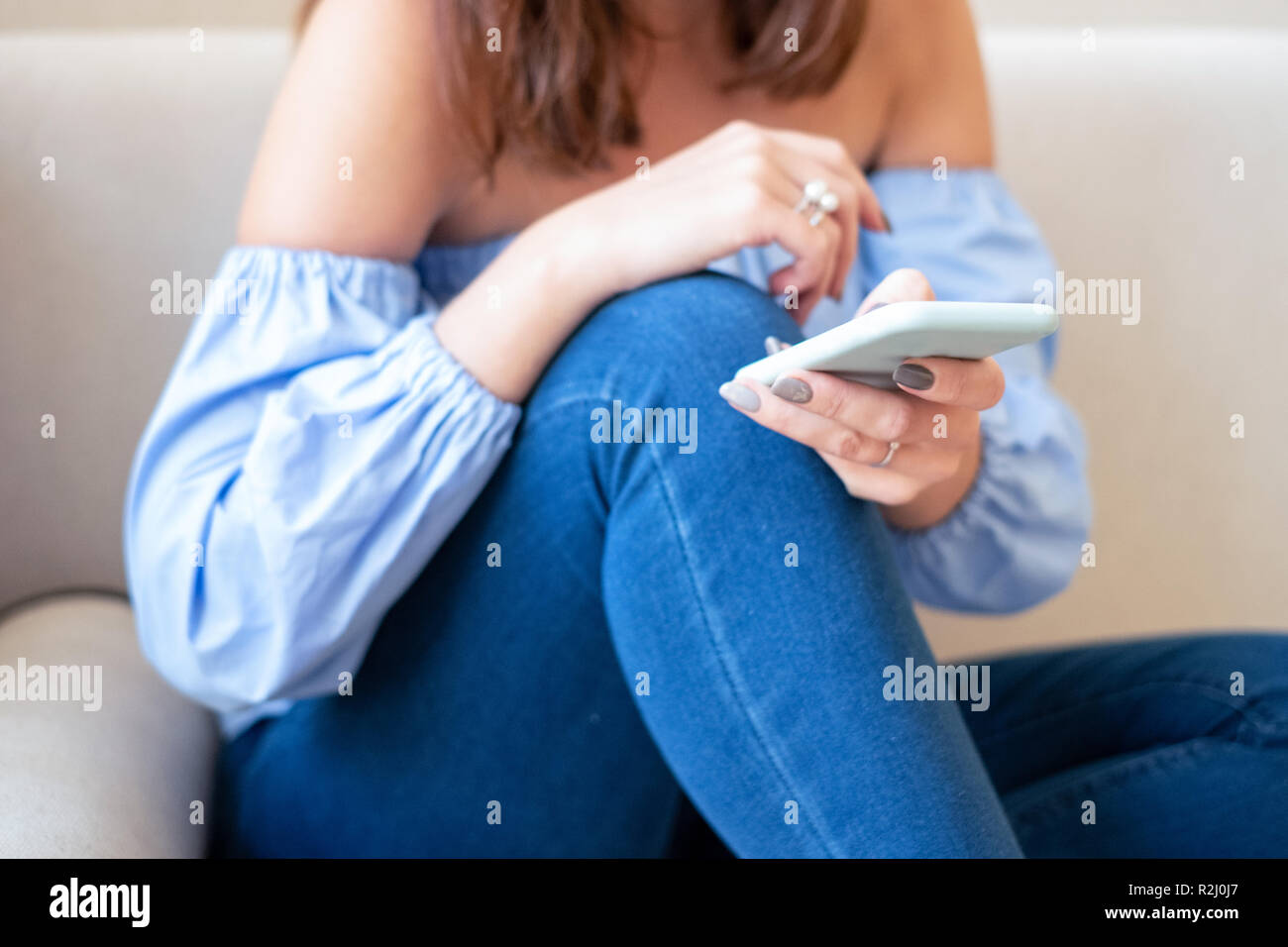 Frau sitzt auf der Couch mit einem Mobiltelefon Stockfoto