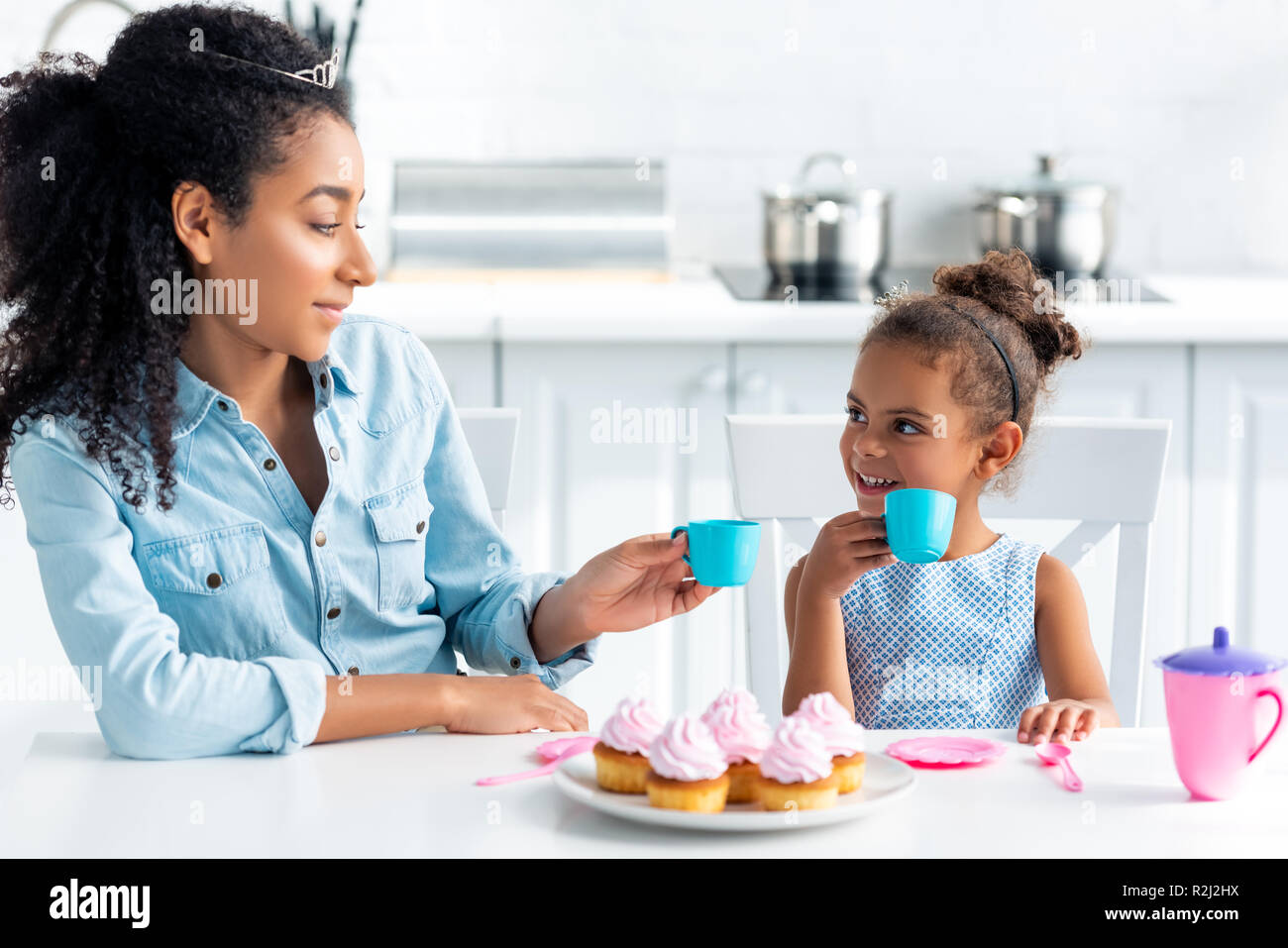 Afrikanische amerikanische Mutter und Tochter mit Tiaras holding Plastikbecher in der Küche Stockfoto