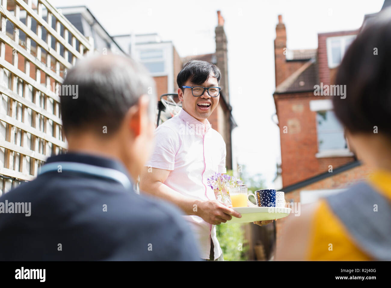 Glücklicher Mann serviert Tee und Saft zur Familie im sonnigen Hof Stockfoto