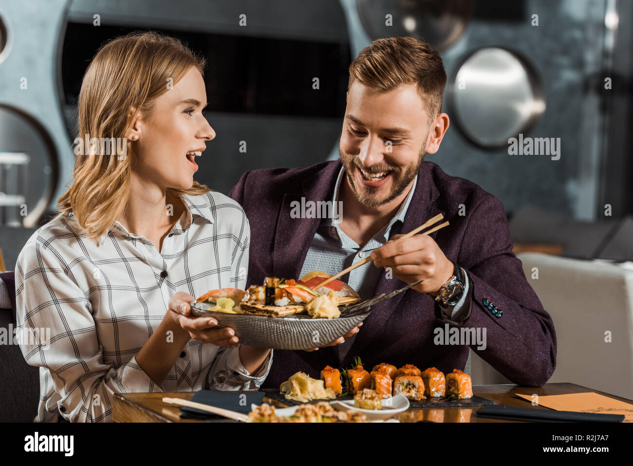 Beautfiful überrascht Frau hält Teller mit leckeren Fisch und Meeresfrüchte, während Paare mit Abendessen in Restaurant Stockfoto