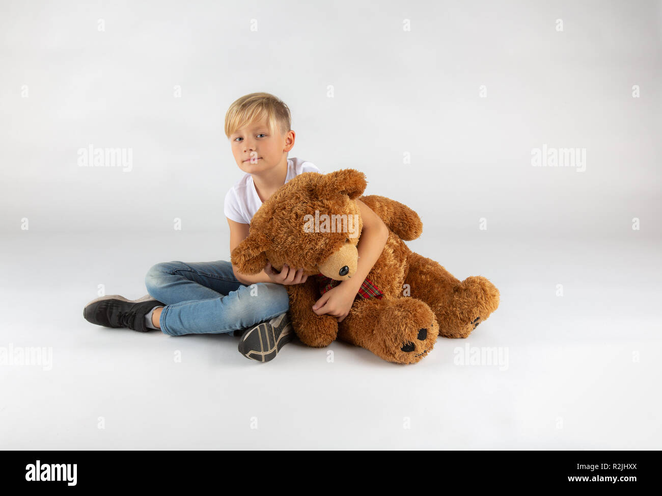 Kleine blonde Junge ist leider auf dem Boden sitzend mit einem großen Teddybär Stockfoto
