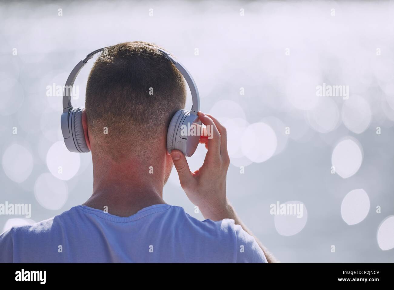 Junger Mann mit Kopfhörern Musik hören gegen Bokeh der Wellen des Meeres. Stockfoto