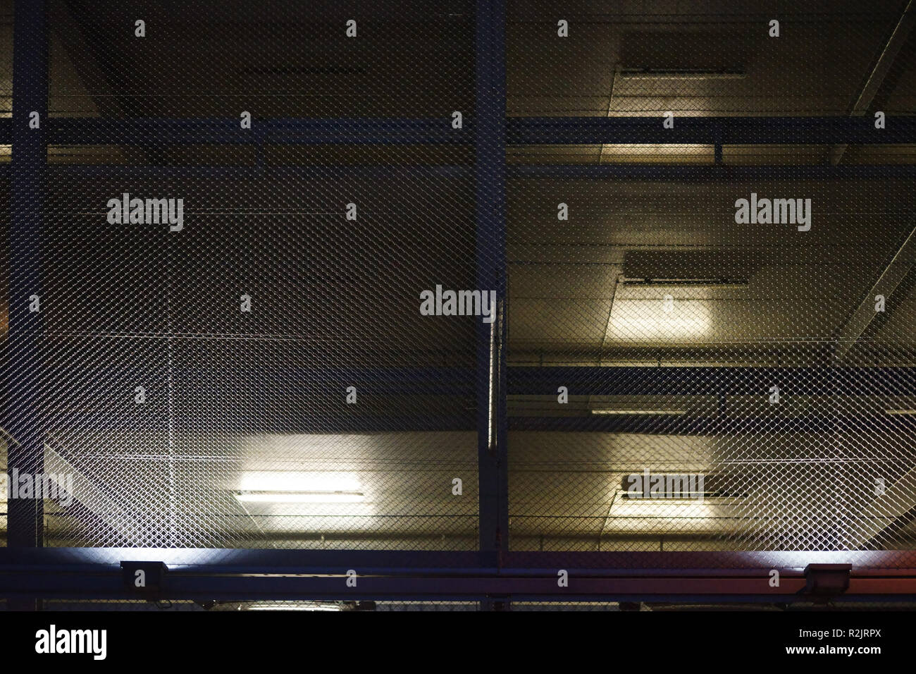 Eine offene Garage mit mehreren Parkdecks durch Gitter Draht geschützt wird nachts beleuchtet Stockfoto