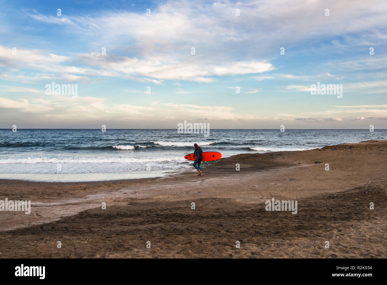 Ein Surfer in Neoprenanzug gehen mit seinem Surfbrett in die Brandung des Meeres. Stockfoto