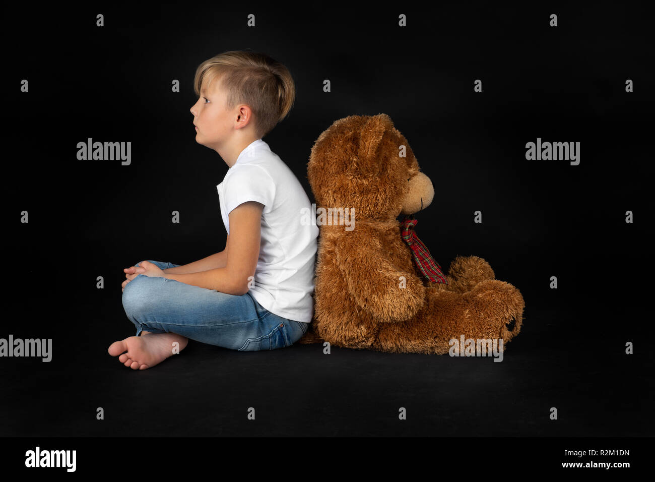 Kleine blonde Junge ist sitzen Rücken an Rücken auf dem Boden und einen großen Teddybären Stockfoto
