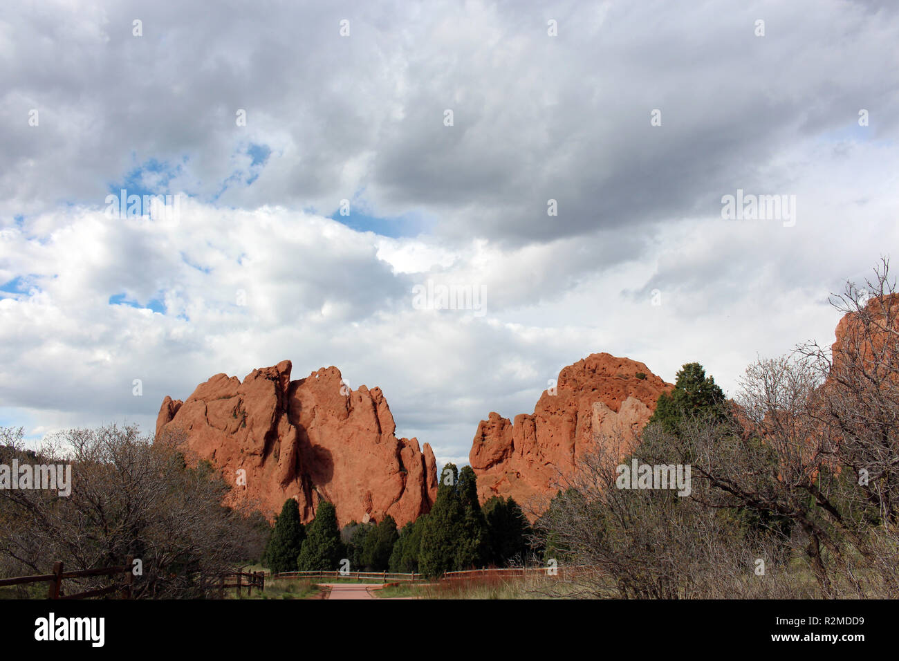 Eine Spur führt zu Red Rock Formationen, die sich hinter Pinien an der Garten der Götter in Colorado Springs, Colorado, USA, bei bewölktem Himmel Stockfoto