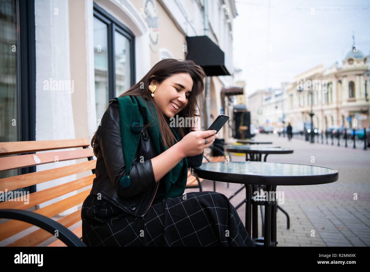 Brunette schöne stilvolle kaukasische Frau in casual Outfit über die europäische Stadt im Cafe eingeben Nachricht auf Ihrem Telefon zu sitzen. Stockfoto