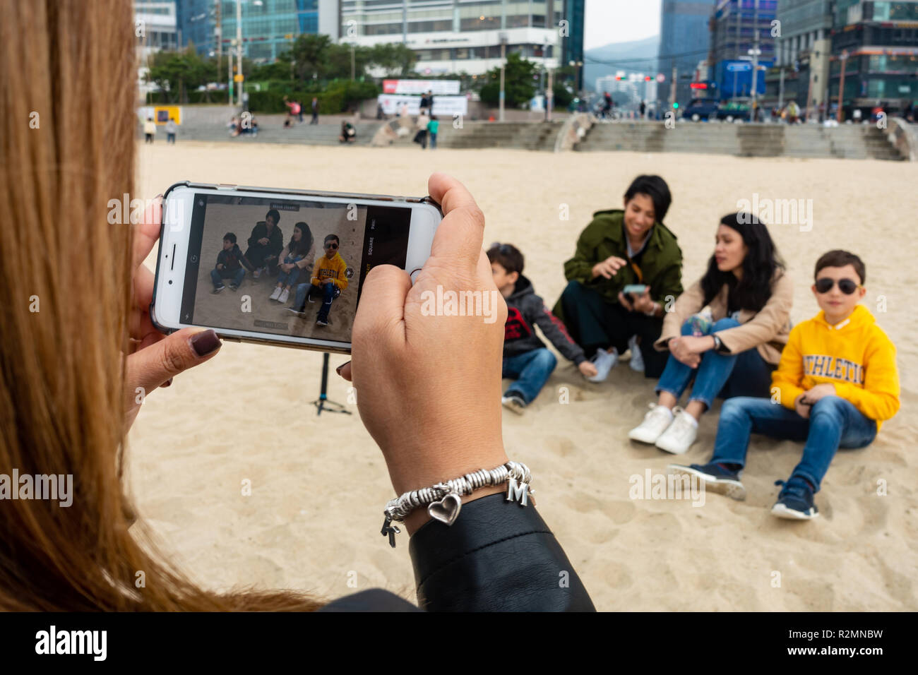 Über die Schulter geschossen von einer Frau ein Foto Ihrer Familie und Freunde mit einem iPhone Handy am Haeundae Beach, Busan, Südkorea Stockfoto