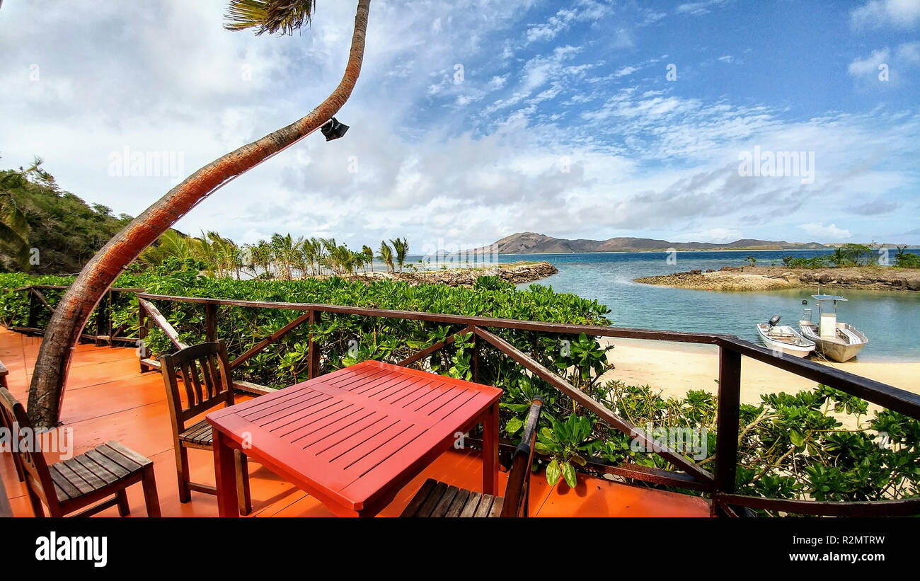 Roter Tisch und Stühle auf der Terrasse am White Sand Beach, zwei Boote im Meer, Fidschi Stockfoto