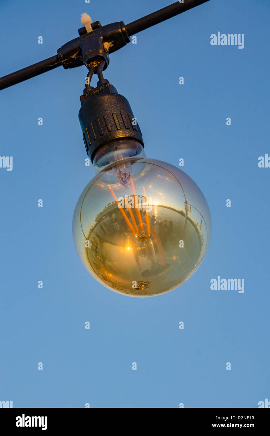 Eine elektrische Glühbirne hängt von einem Strom Kabel, dargestellt im Freien vor einem blauen Himmel. Stockfoto