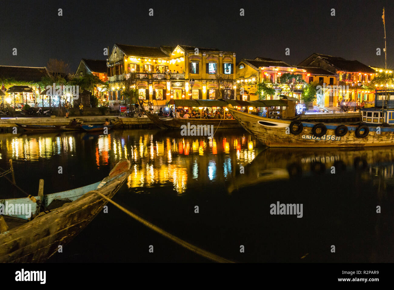 Beleuchtet, historische Altstadt von Hoi An, von den gegenüberliegenden Flußufer, Laternen auf dem Wasser spiegelt, Boote im Vordergrund. Stockfoto