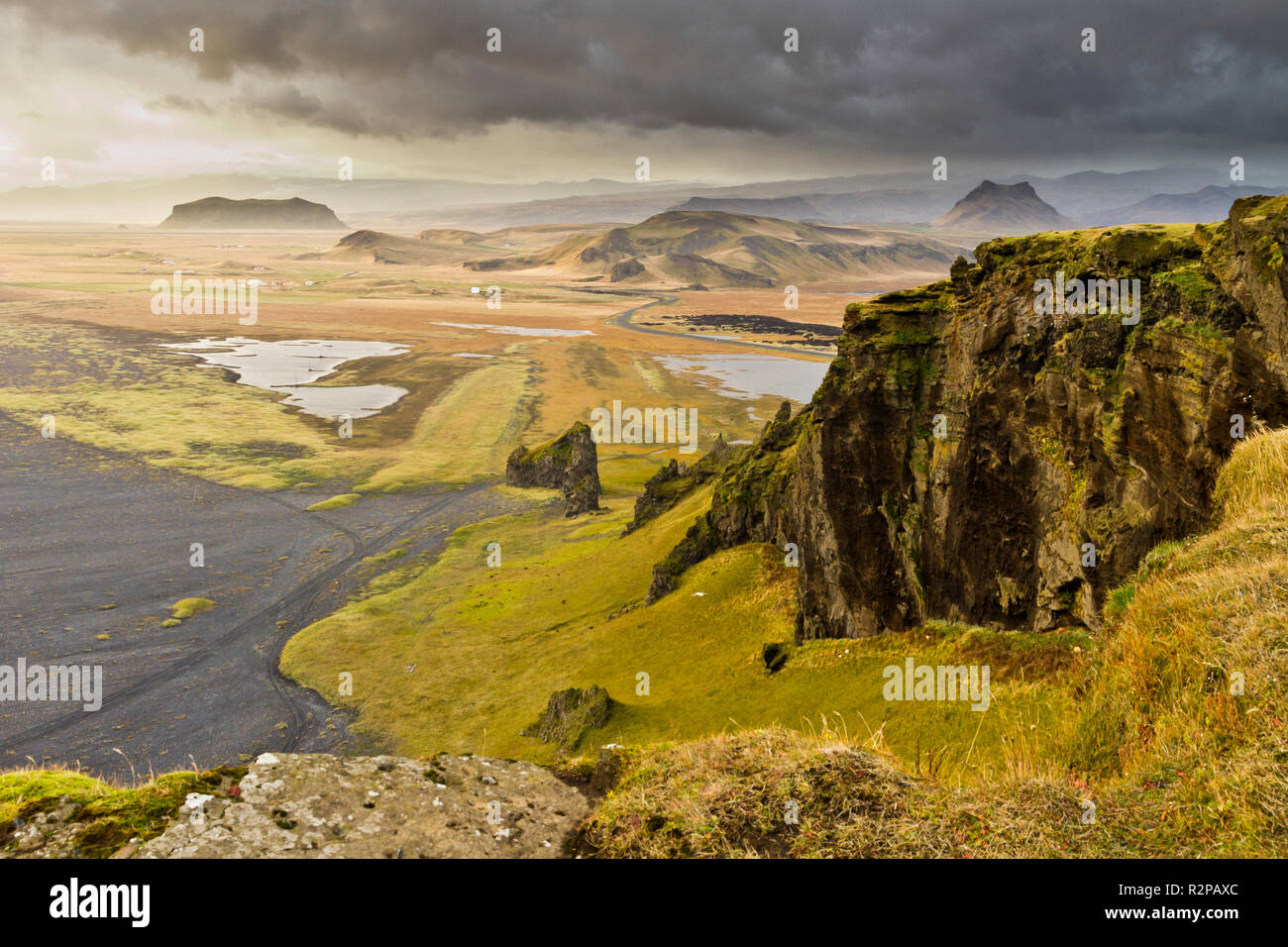 Blick auf die spektakuläre isländische Landschaft mit dramatischen Wolken, grüne Wiesen, schwarzen Strand und schroffe Felsen Stockfoto