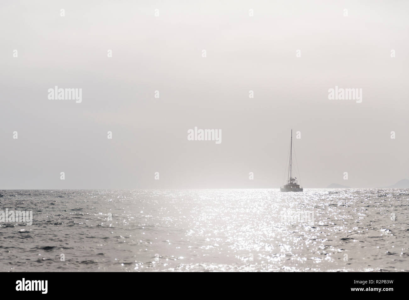 Einfarbig grau, minimalistischen Bild von einem Segelboot auf dem offenen Meer, Hell glitzert in der Sonne Stockfoto