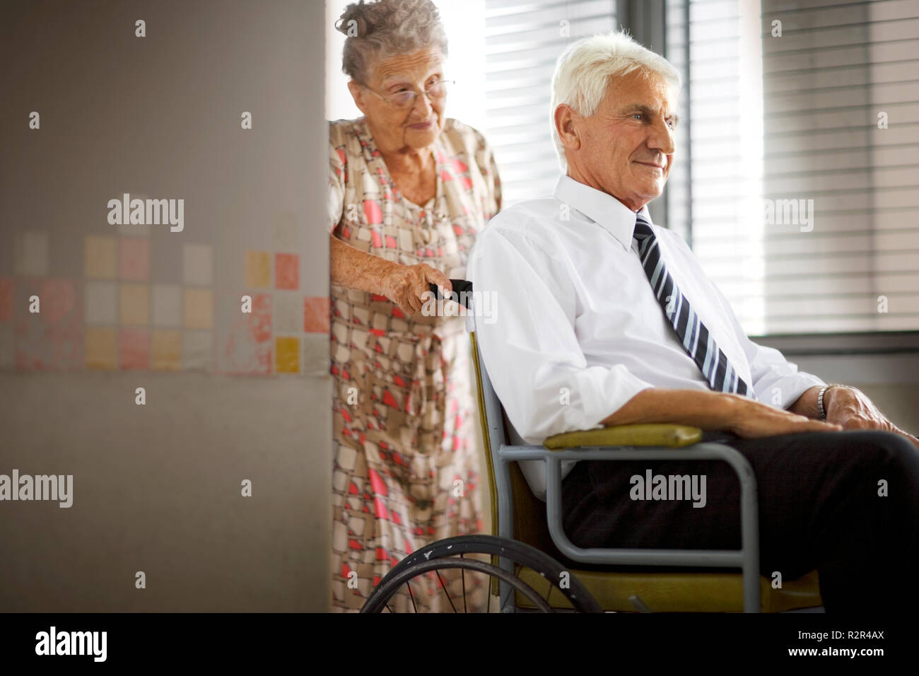 Eine ältere Frau drückt einen älteren Mann in einem Rollstuhl. Stockfoto