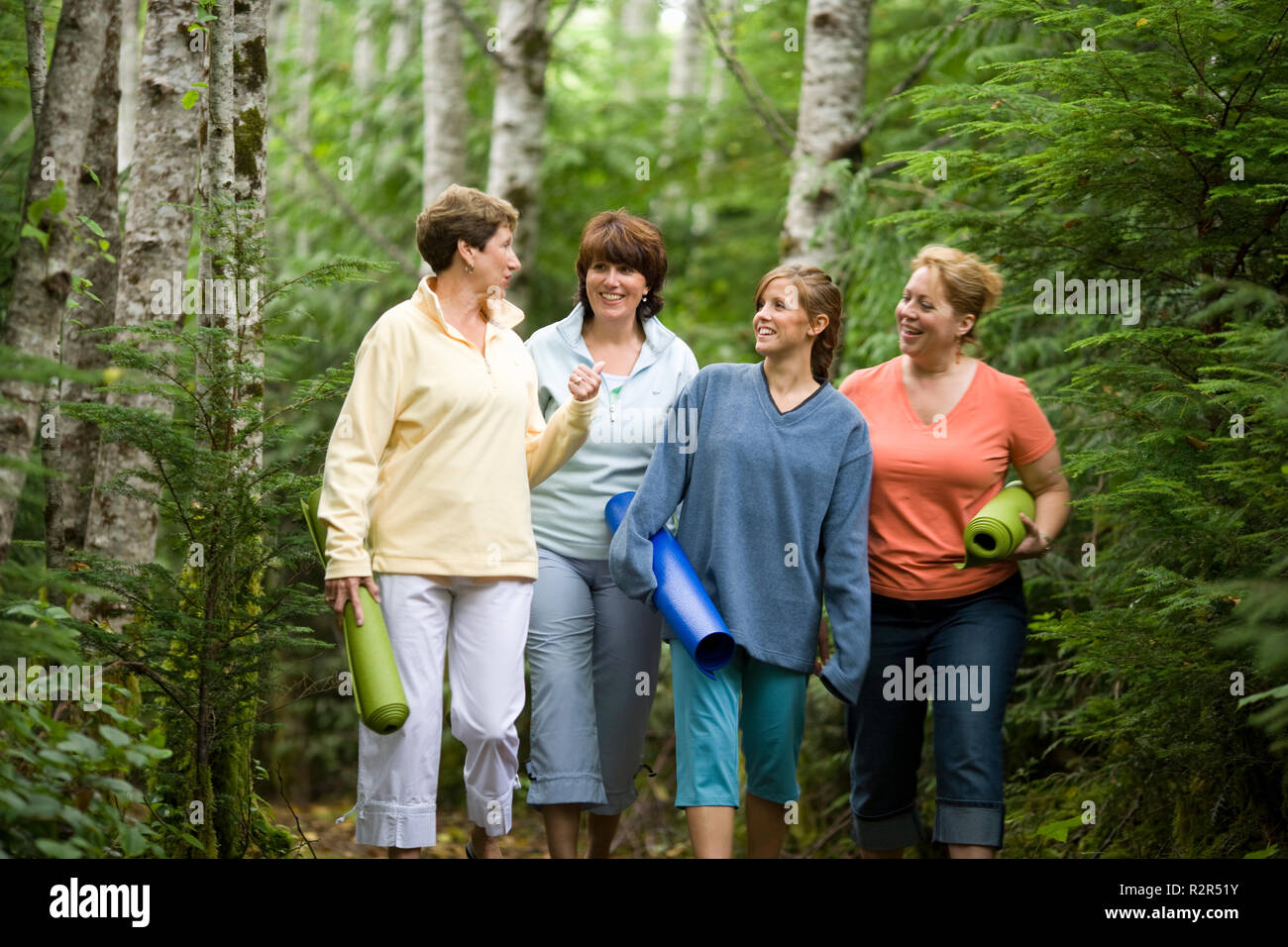 Junges Mädchen mit zwei erwachsenen Frau und eine reife Frau gehen mit Yogamatten durch den Busch. Stockfoto