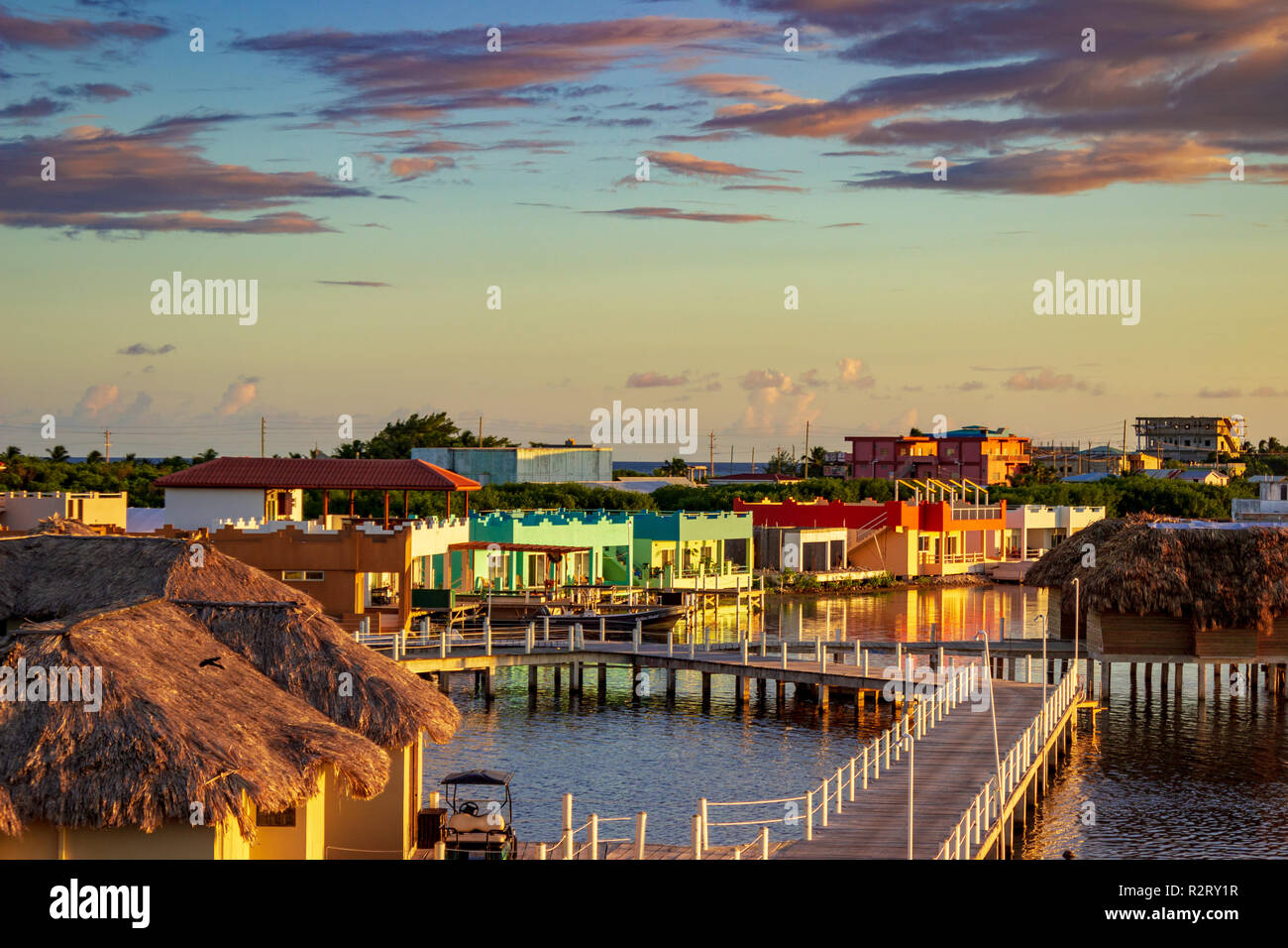 Über Wasser Cabanas und Fahrstraßen zeichnen sich inmitten der bunten Häusern von San Pedro, Ambergris Caye, Belize bei Sonnenuntergang. Stockfoto