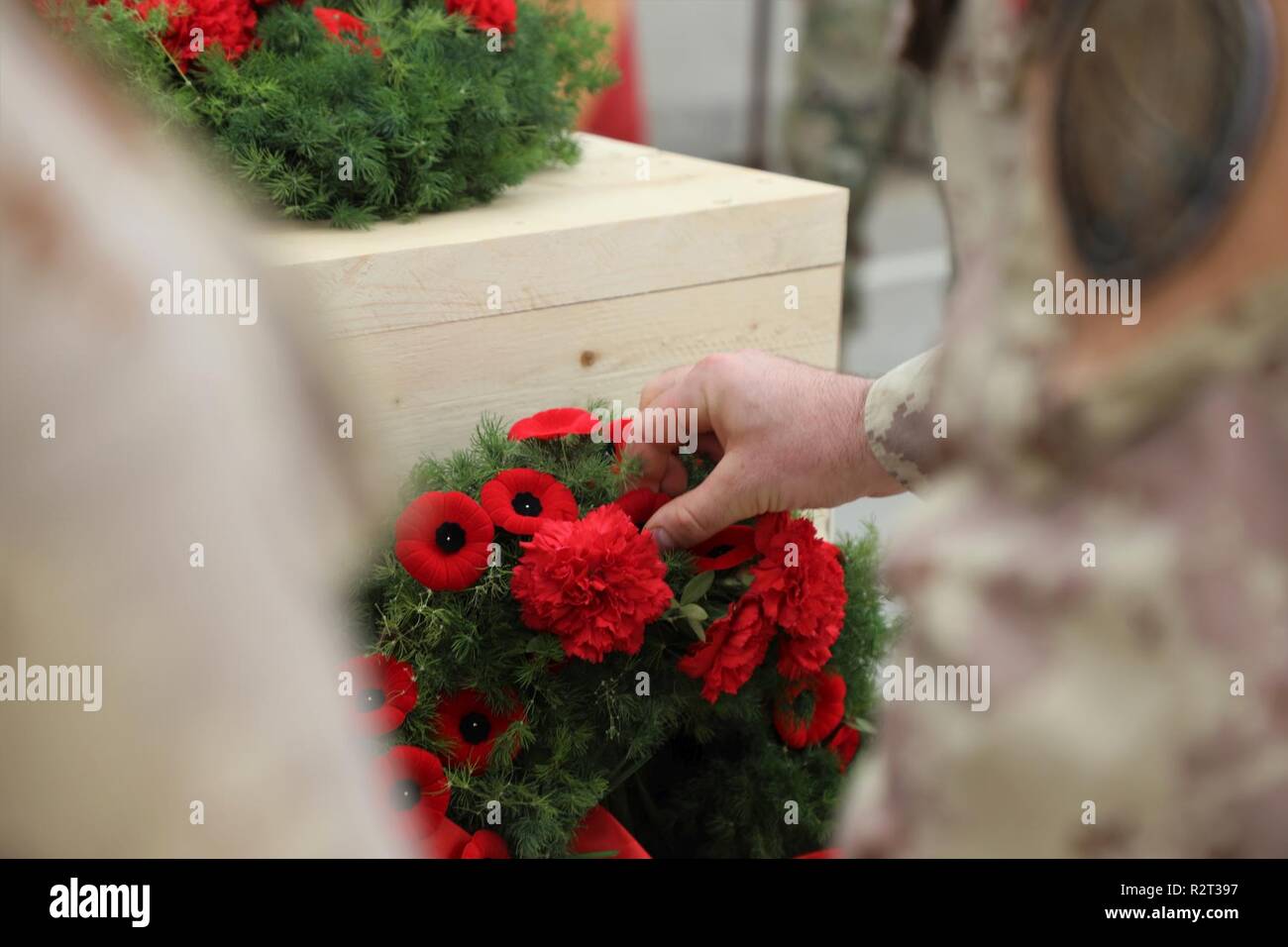 Ein kanadischer Offizier pins Eine Mohnblüte Revers zu einem Memorial Kranz auf eine Armistice Day Zeremonie an Union III, Bagdad an November 11, 2018. Armistice Day wird jährlich beobachtet am 07.11.11 und fällt mit Veteranen Tag und Tag der Erinnerung. Veteranen Tage ehrt alle amerikanischen Veteranen, und der Tag des Gedenkens ehrt die Mitglieder der Streitkräfte, die starben, während in der Linie der Aufgabe dienen. Heute ist die globale Koalition zu besiegen ISIS auf 74 Mitgliedstaaten und fünf internationalen Organisationen gewachsen und spiegelt die internationale Engagement für die Mission. Stockfoto