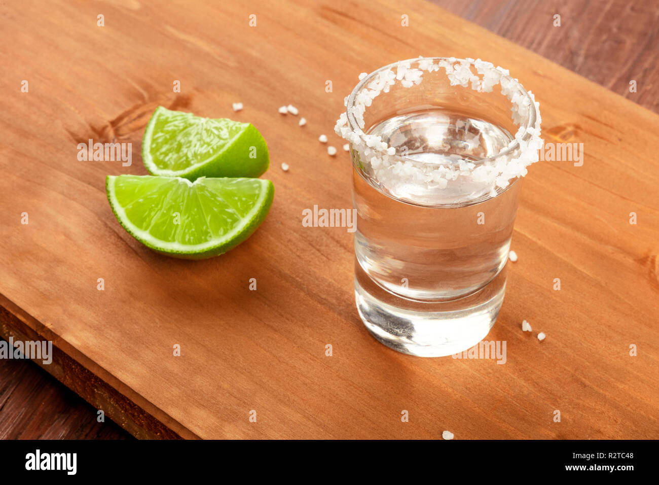 Ein tequila Shot mit gesalzenem Rim und Kalk Schichten auf einem dunklen Holzmöbeln im Landhausstil Hintergrund Stockfoto