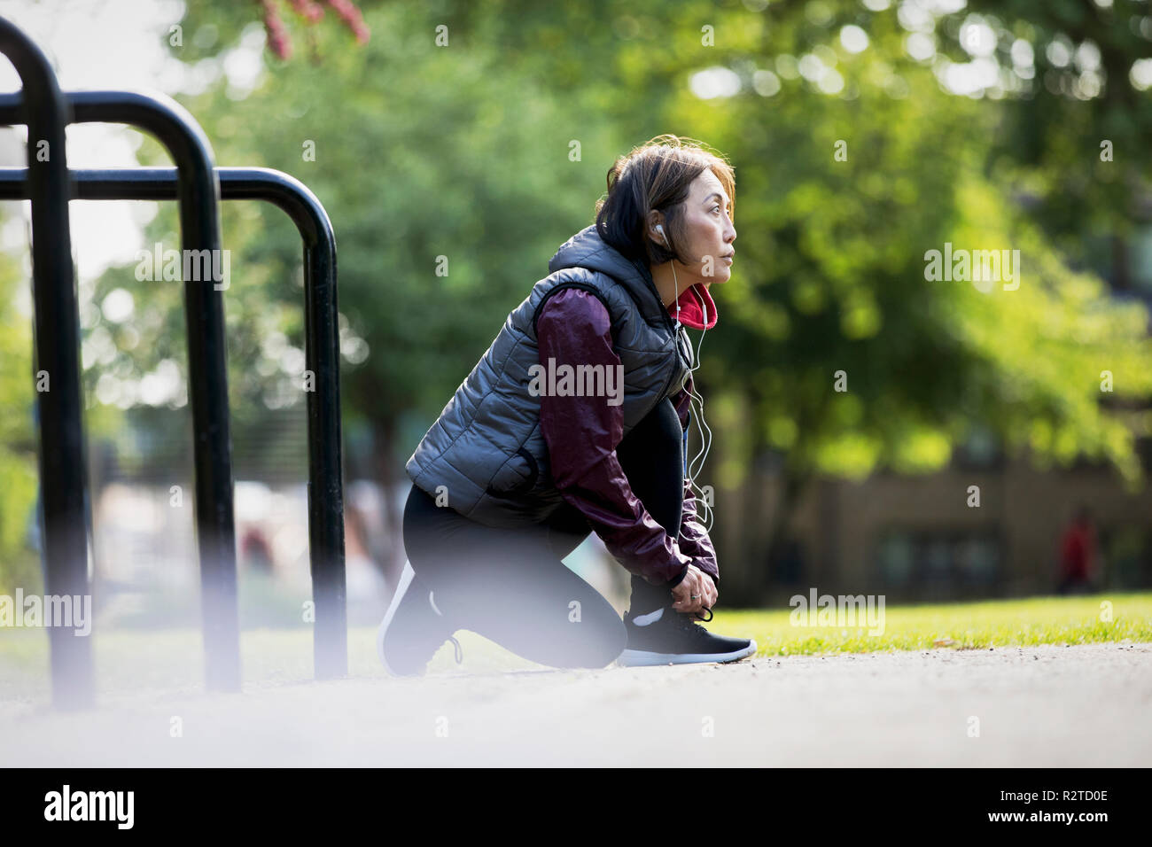 Active Senior Läuferin mit Kopfhörern Schuh binden in Park Stockfoto
