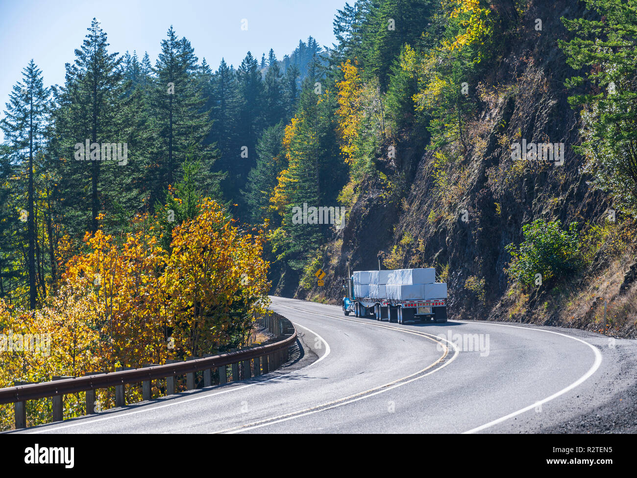 Big Rig blau klassische amerikanische Motorhaube Long Haul Semi Truck Transport von Schnittholz auf die beiden flachbett Auflieger auf die Umdrehung der Wicklung aut läuft Stockfoto