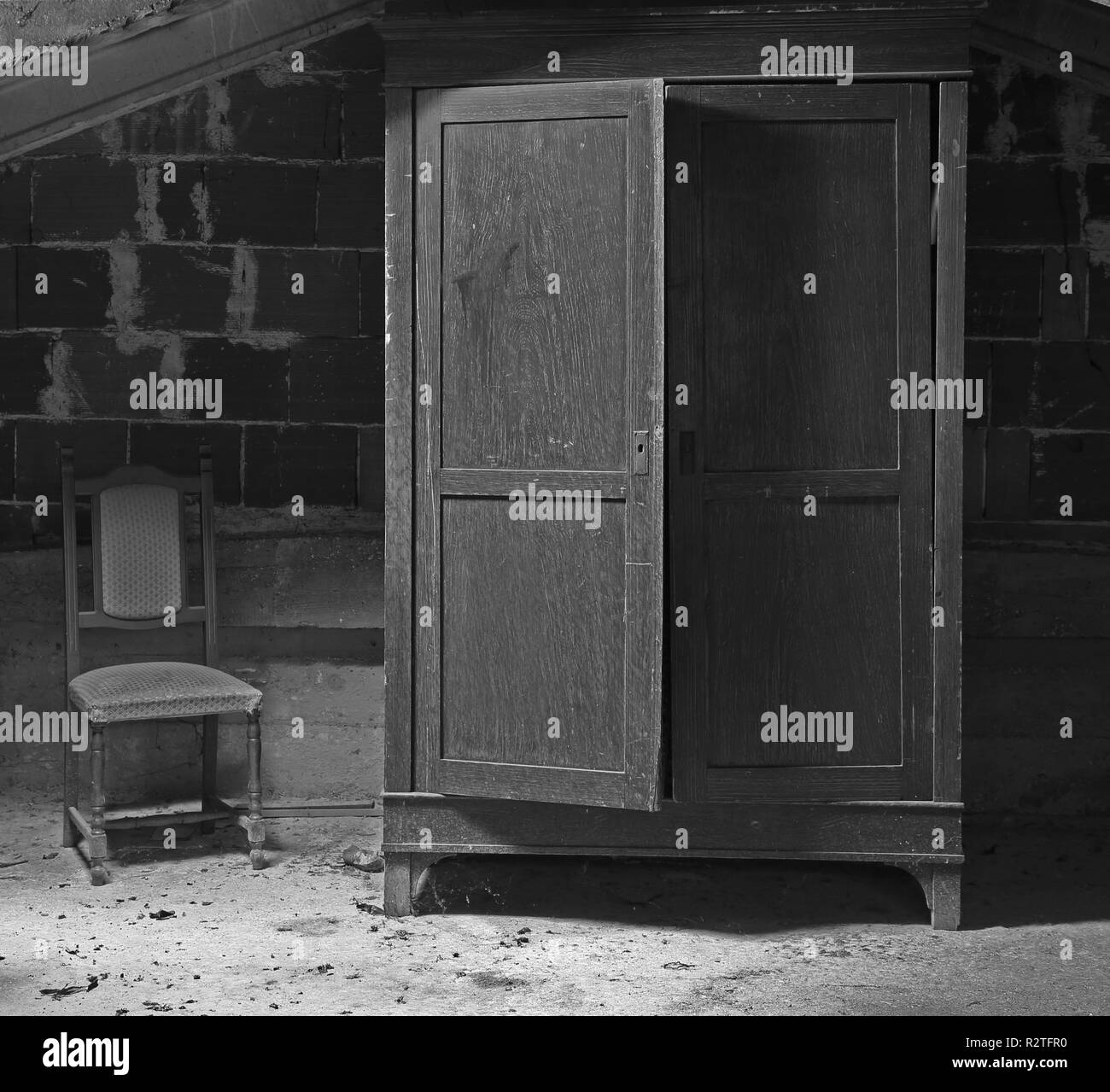 Sehr alte scary Schrank in der staubigen Dachboden mit einem kaputten Stuhl neben mit Schwarzweiß-Effekt Stockfoto