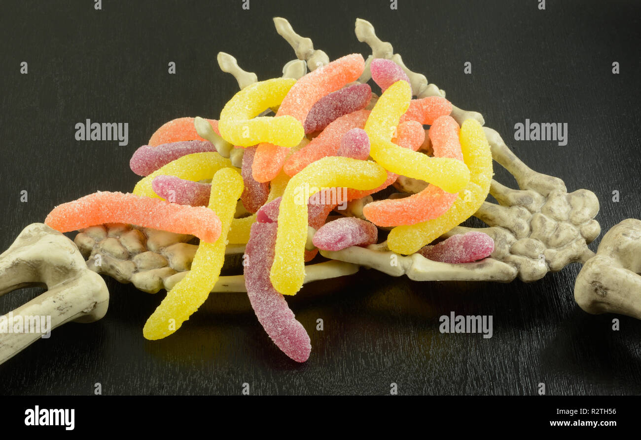 Halloween Skelett Hände halten Süßigkeiten Gummibärchen Worms auf schwarzem Holz- Hintergrund Stockfoto